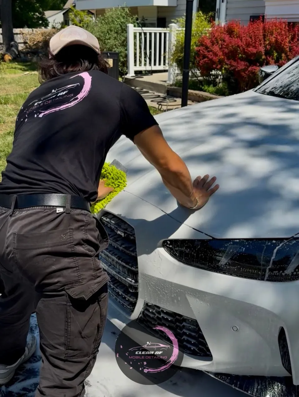 Clean AF detailer in a branded shirt working on the hood of a white BMW