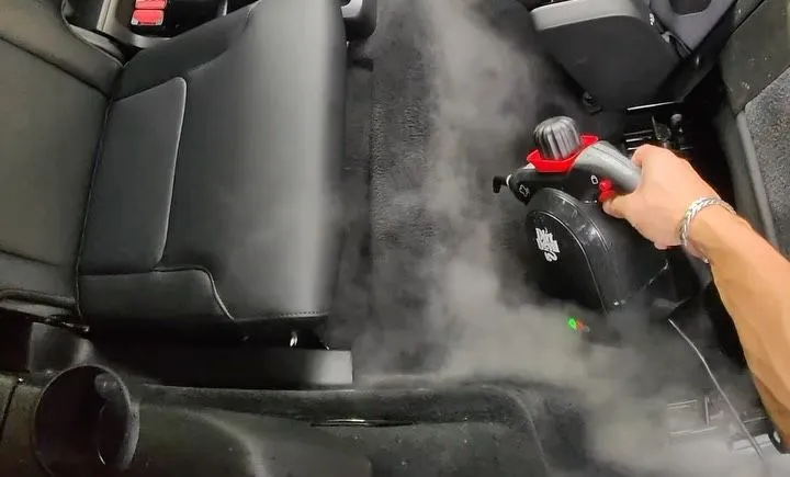 Steam cleaner working on a rear carpet during an interior detail